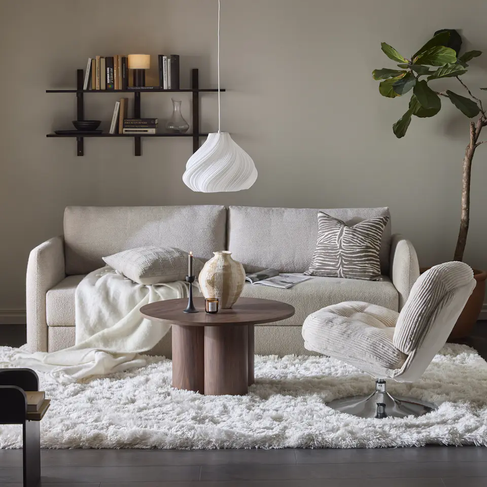 En beige soffa står i ett vardagsrum tillsammans med en vit matta och en beige fåtölj