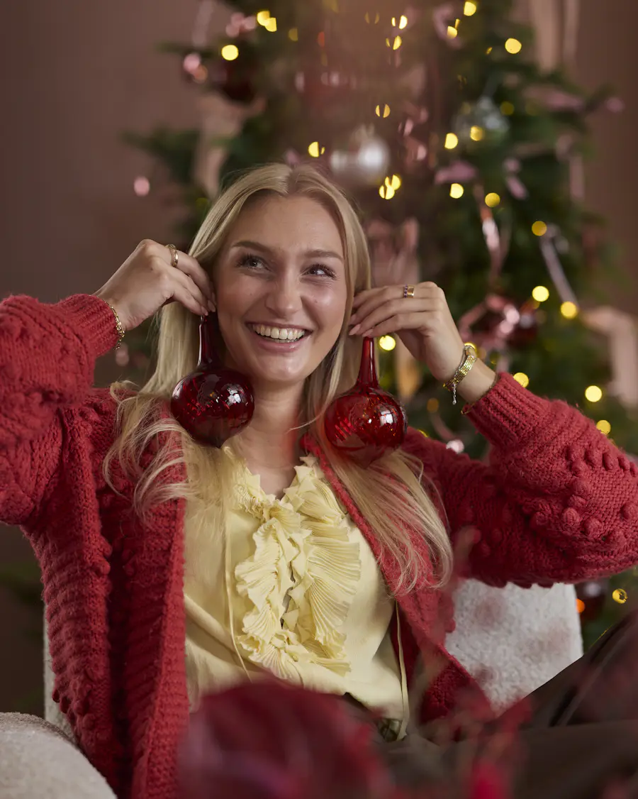 En blond tjej håller upp julgransdekoration vid öronen.