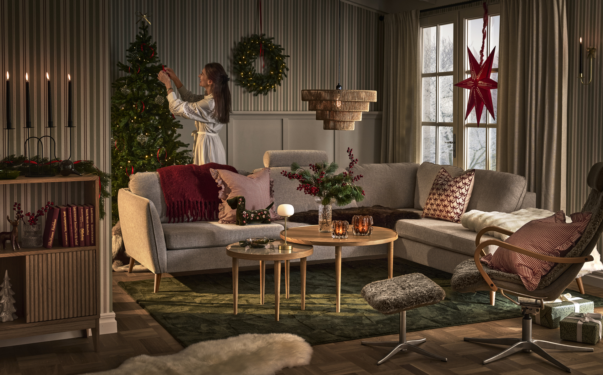 En tjej står bakom en soffa i ett vardagsrum och pyntar en julgran.