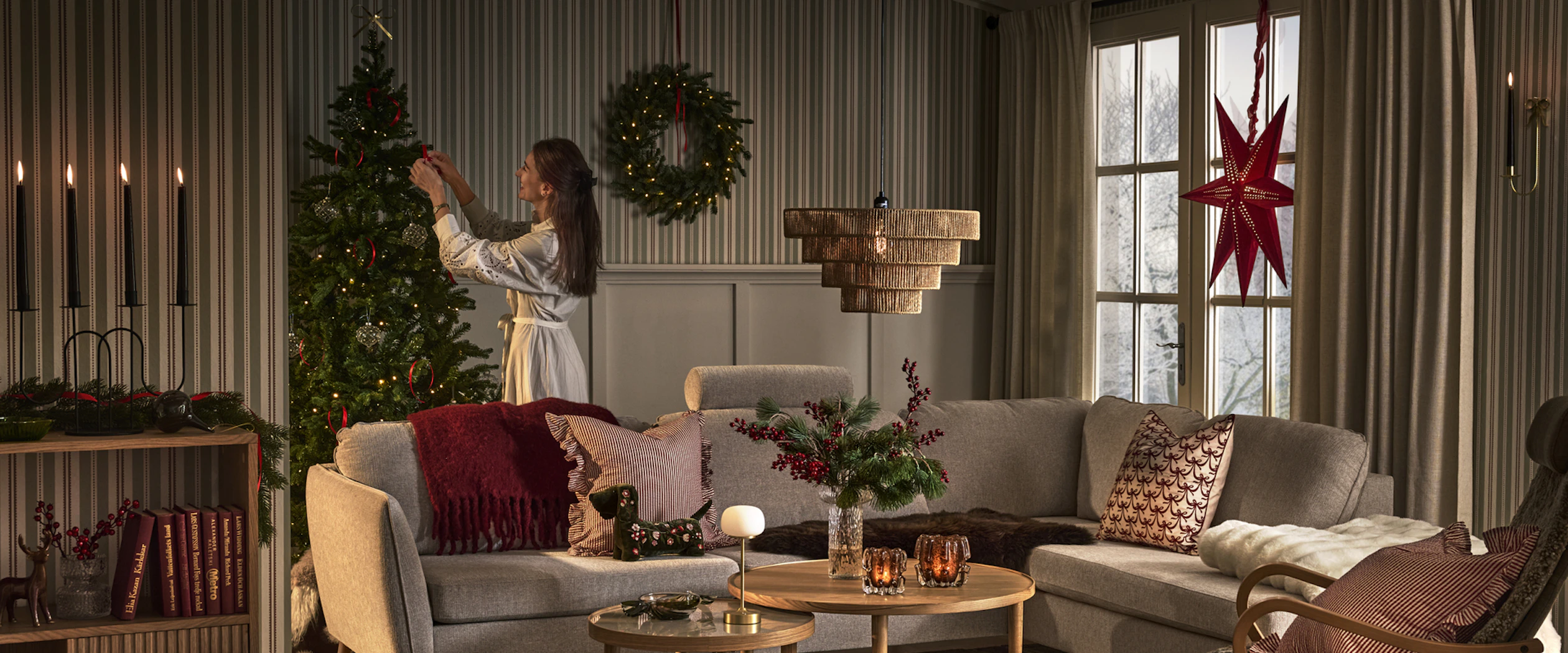 En tjej står bakom en soffa i ett vardagsrum och pyntar en julgran.