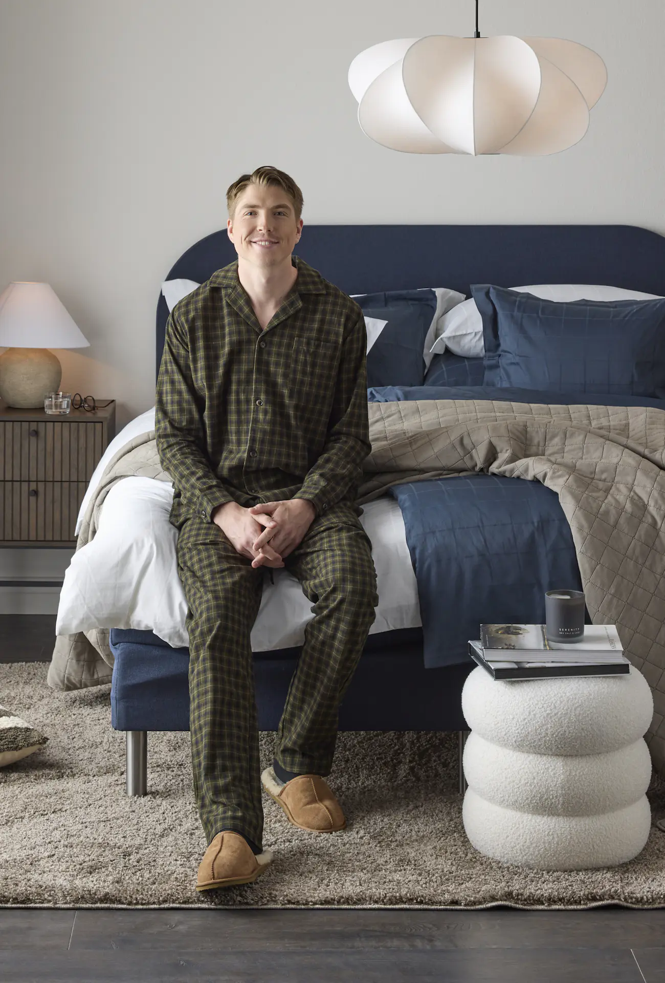 William Poromaa som är längdskidåkare i svenska landslaget och Mios sömnambassadör sitter vid fotändan på en kontinentalsäng i blått tyg iklädd mörk grön rutig pyjamas.