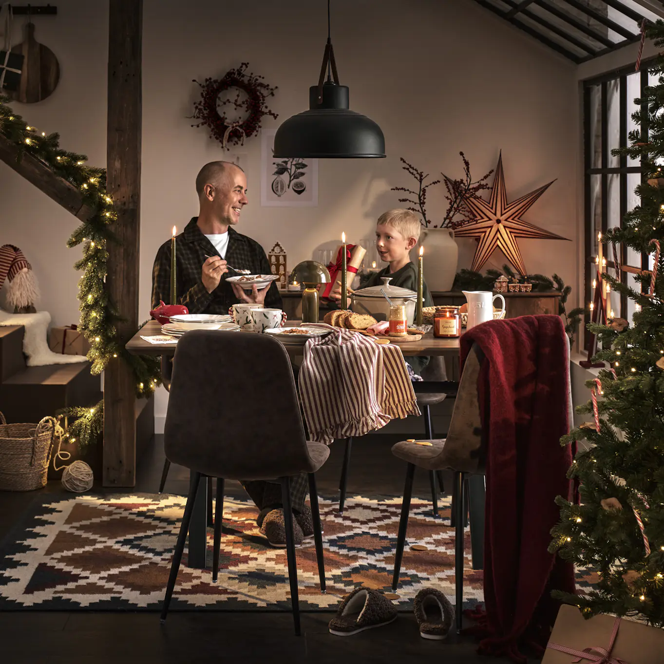 En man och en pojke sitter vid ett matbord i ett julpyntat kök.