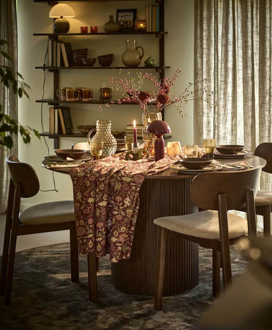 Höstdukat runt mörbrunt bord med vinröd blommig duk och fyra matchande stolar.