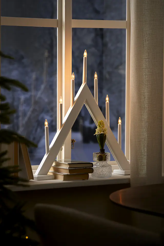 I ett fönster står en vit adventsljusstake och en hyacint. Till vänster om fönstret skymtas en julgran.