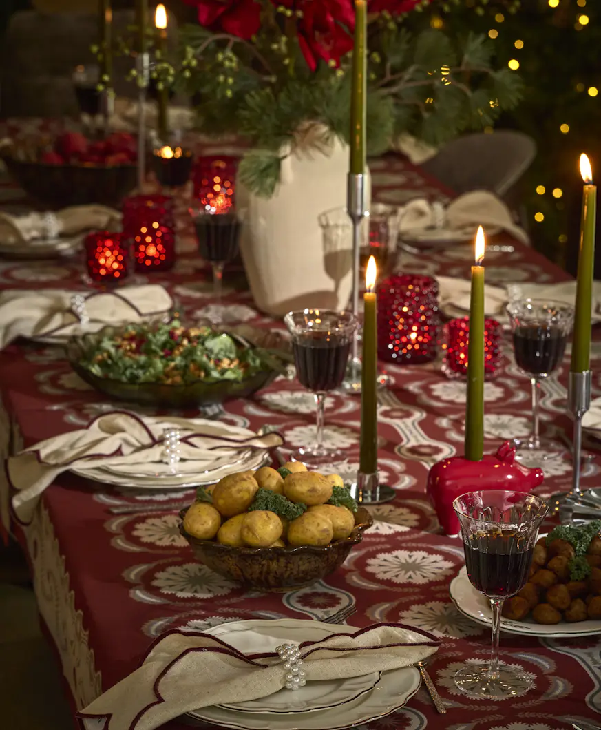 Ett juldukat matbord med glas och porslin, ljus samt blommor.