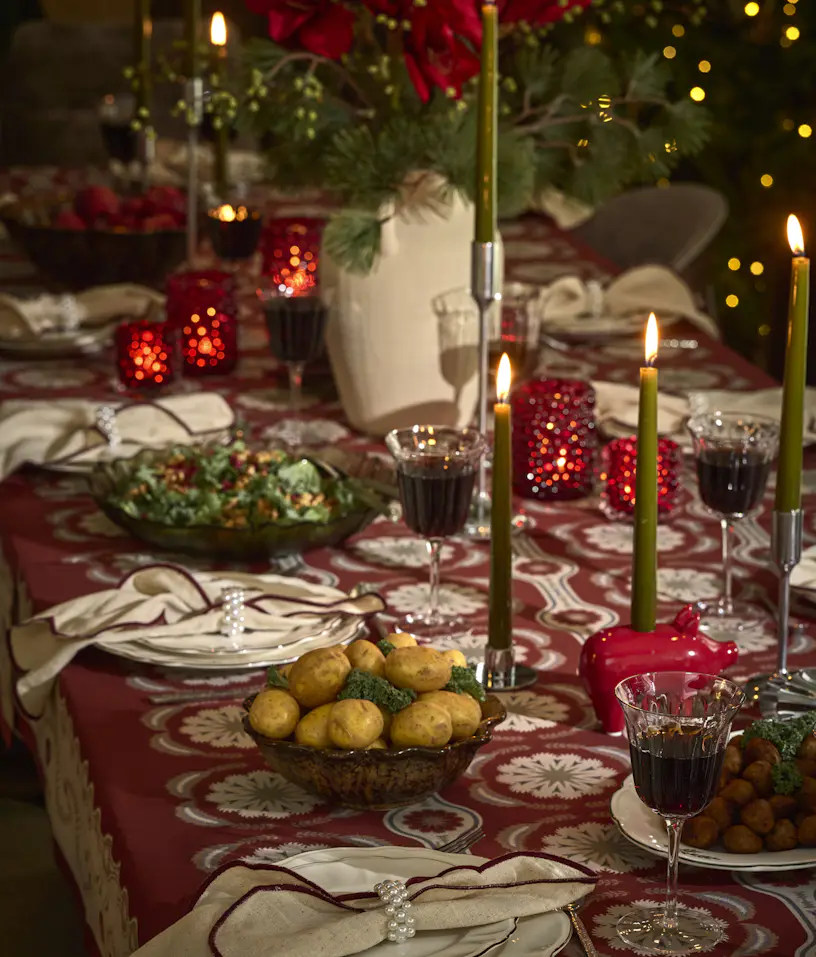 Ett juldukat matbord med glas och porslin, ljus samt blommor.