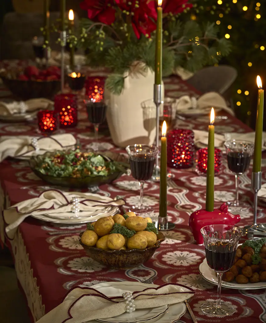 Ett juldukat matbord med glas och porslin, ljus samt blommor.