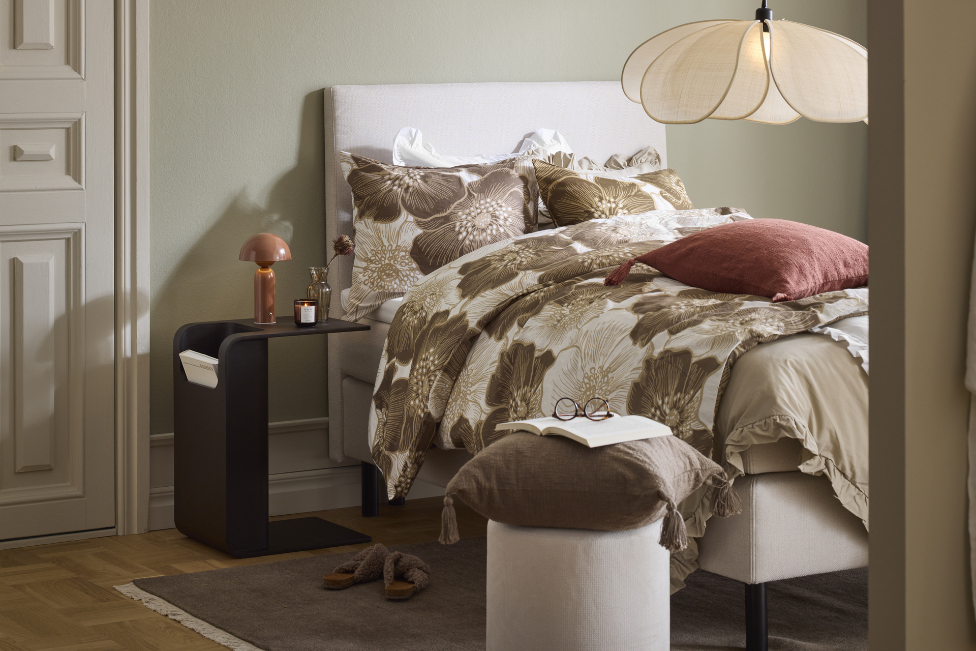 Beige enkelsäng bäddad med påslakan i jordnära toner står i ett sovrum med gröna väggar.