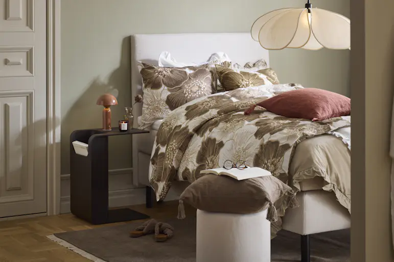 Beige enkelsäng bäddad med påslakan i jordnära toner står i ett sovrum med gröna väggar.