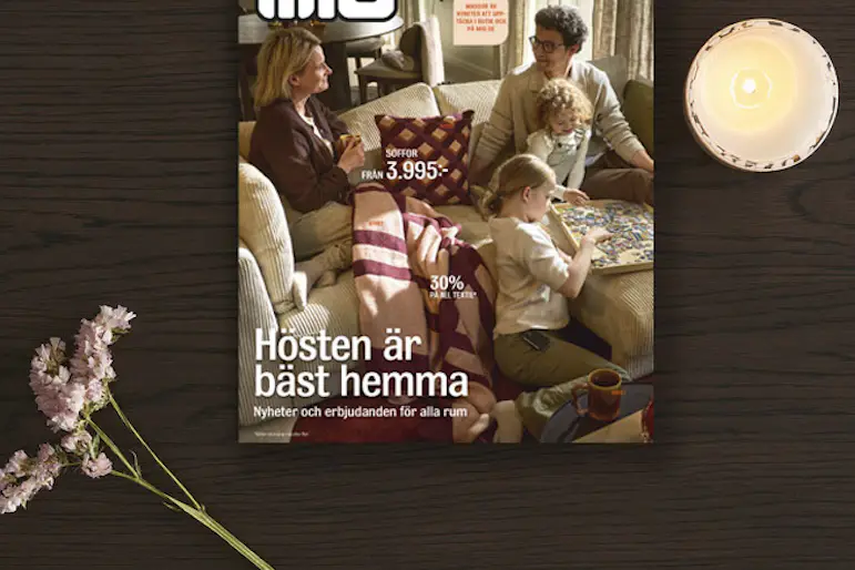 Kampanjblad ligger på ett mörkt träbord tillsammans med en blomma och ett ljus.