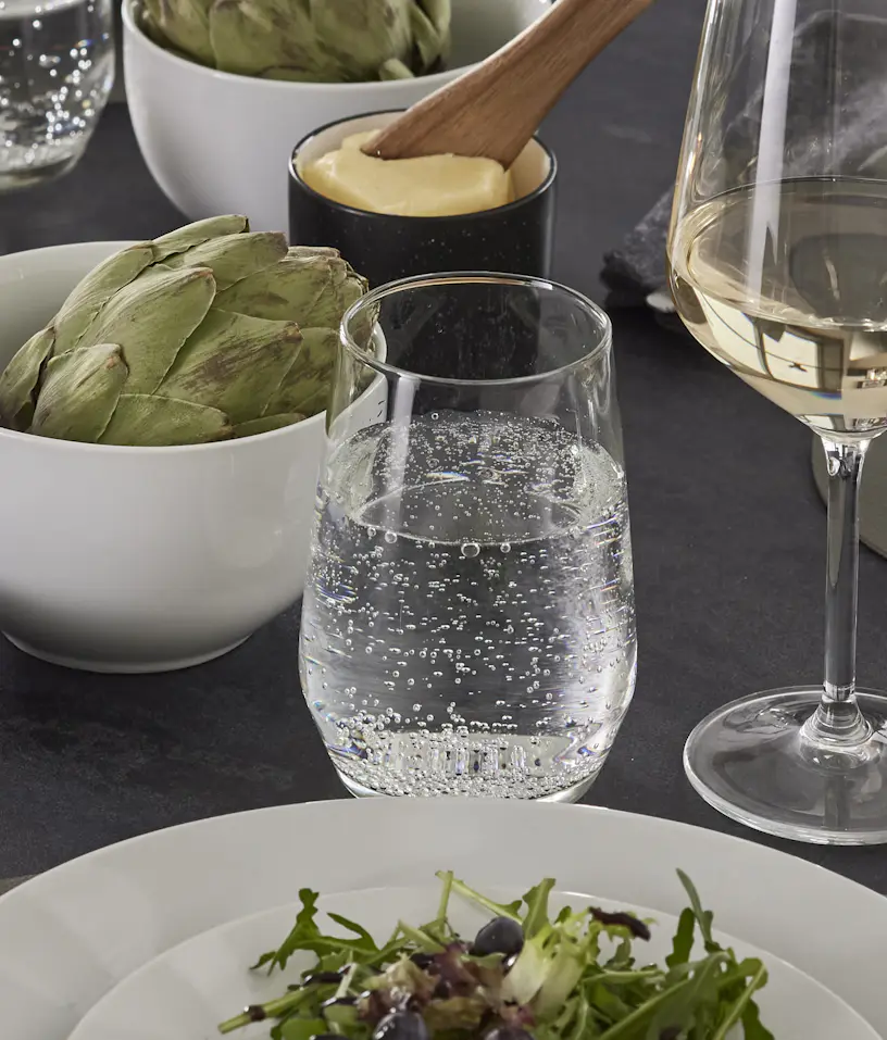 Glas med bubbelvatten står vid ett vinglas, en tallrik med sallad och en skål med kronärtskocka.