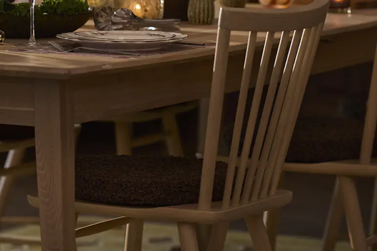 I ett vardagsrum står ett rektangulärt träbord med sex tillhörande stolar. Från taket hänger en taklampa. I bakgrunden syns ett sällskap.