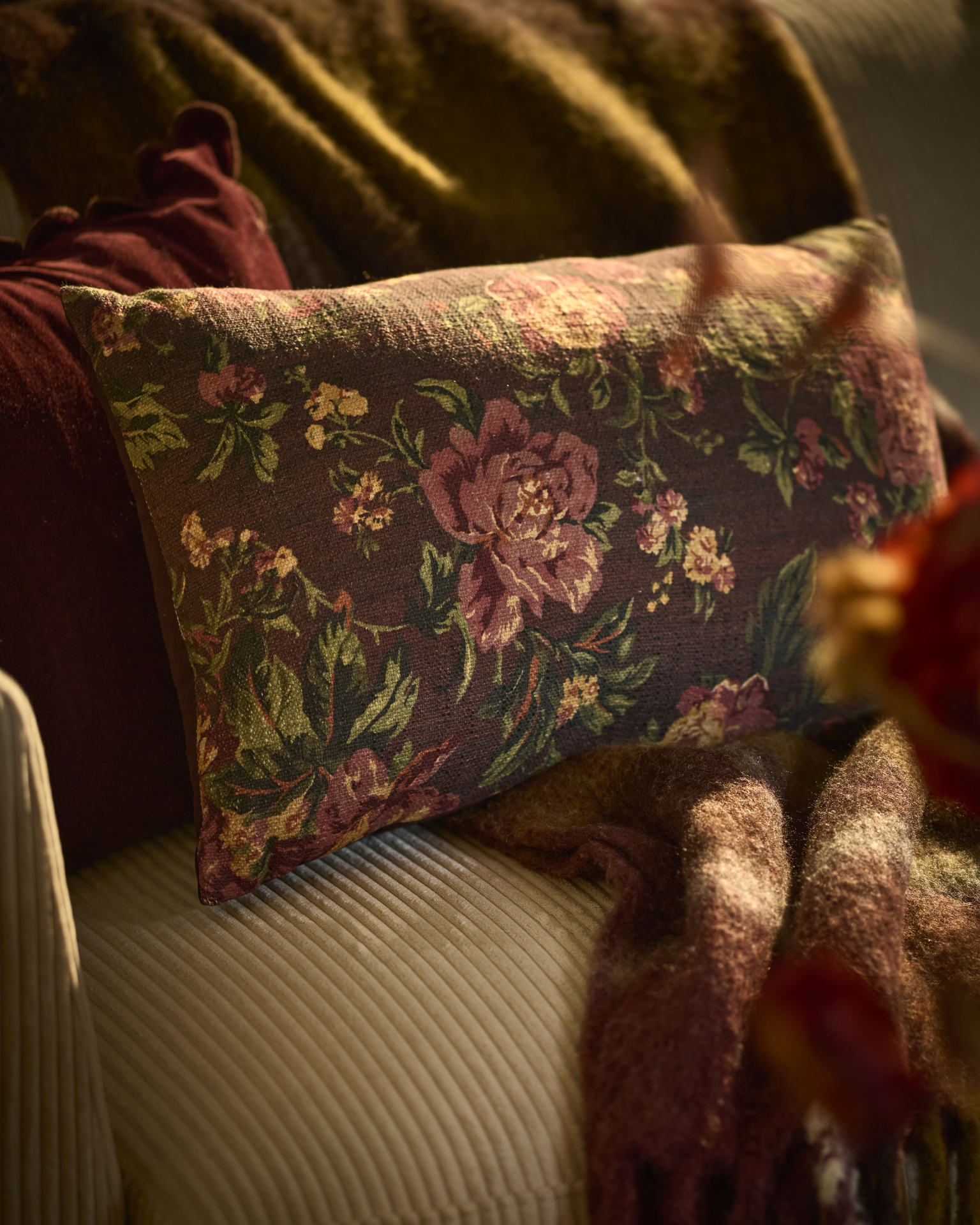 En brun prydnadskudde med blommönster ligger på en beige soffa