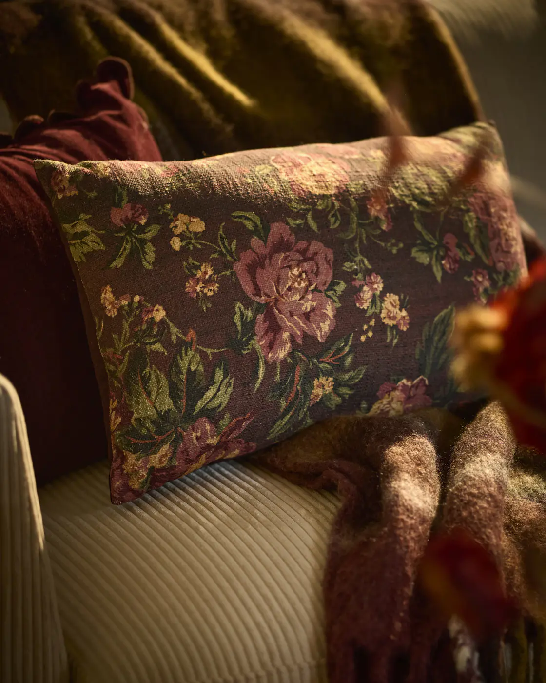 En brun prydnadskudde med blommönster ligger på en beige soffa
