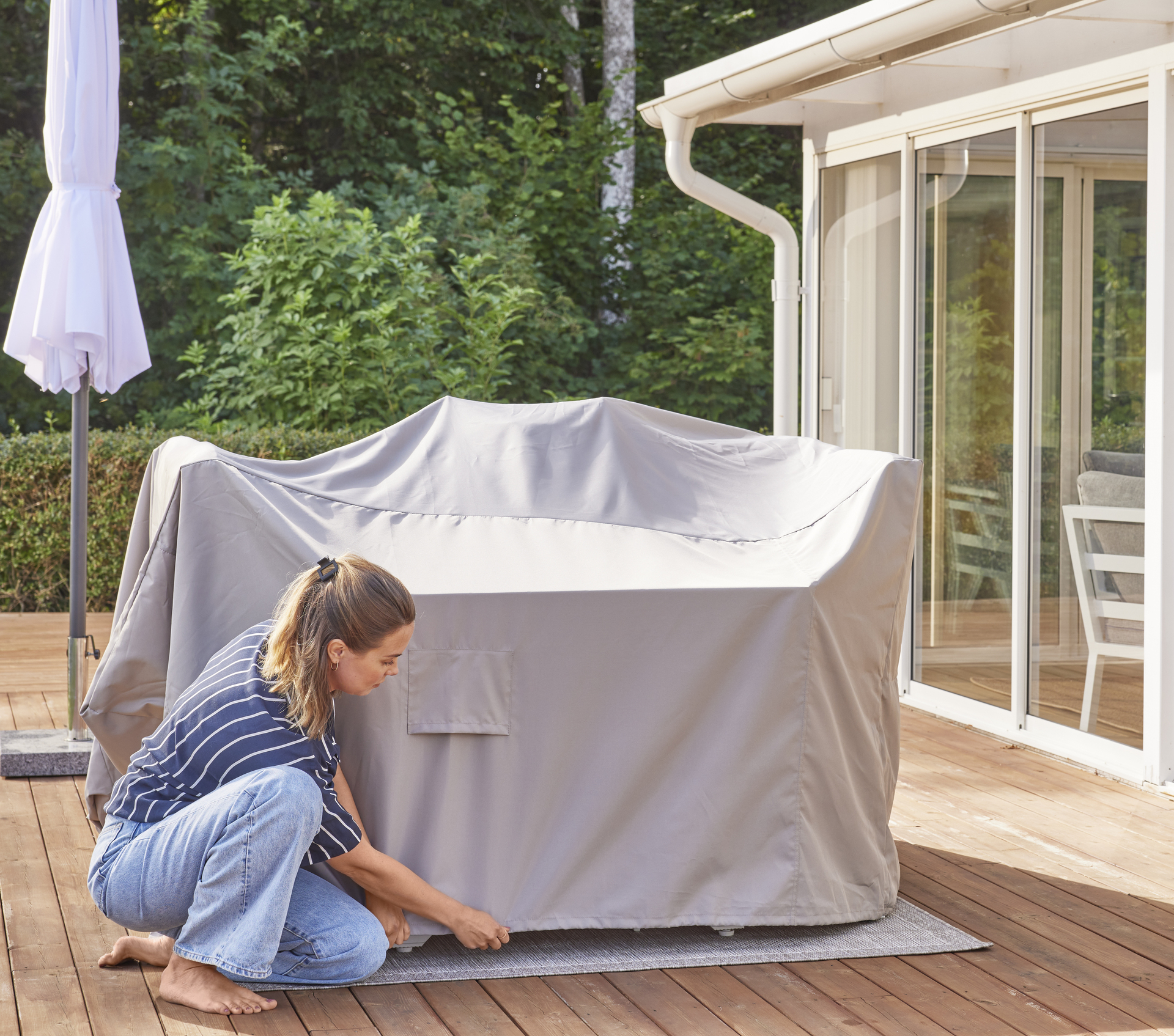 På en altan sätter en kvinna på ett möbelöverdrag över en utemöbelsgrupp