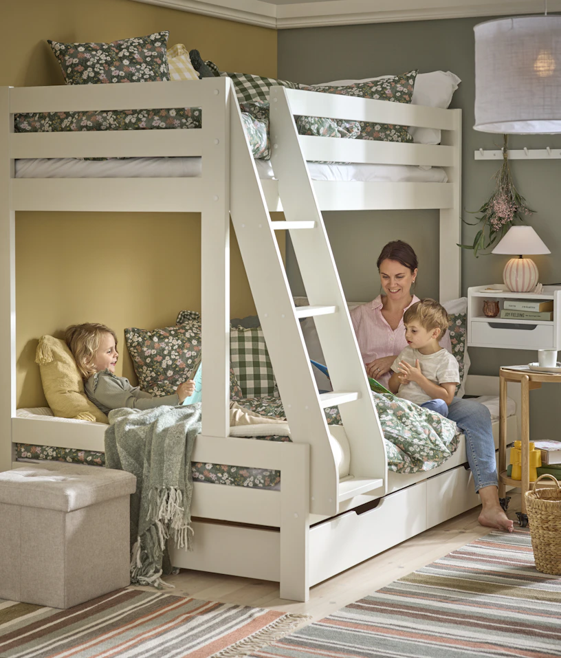 Mamma med två barn sitter i under våningen på en vit våningssäng med en stege.