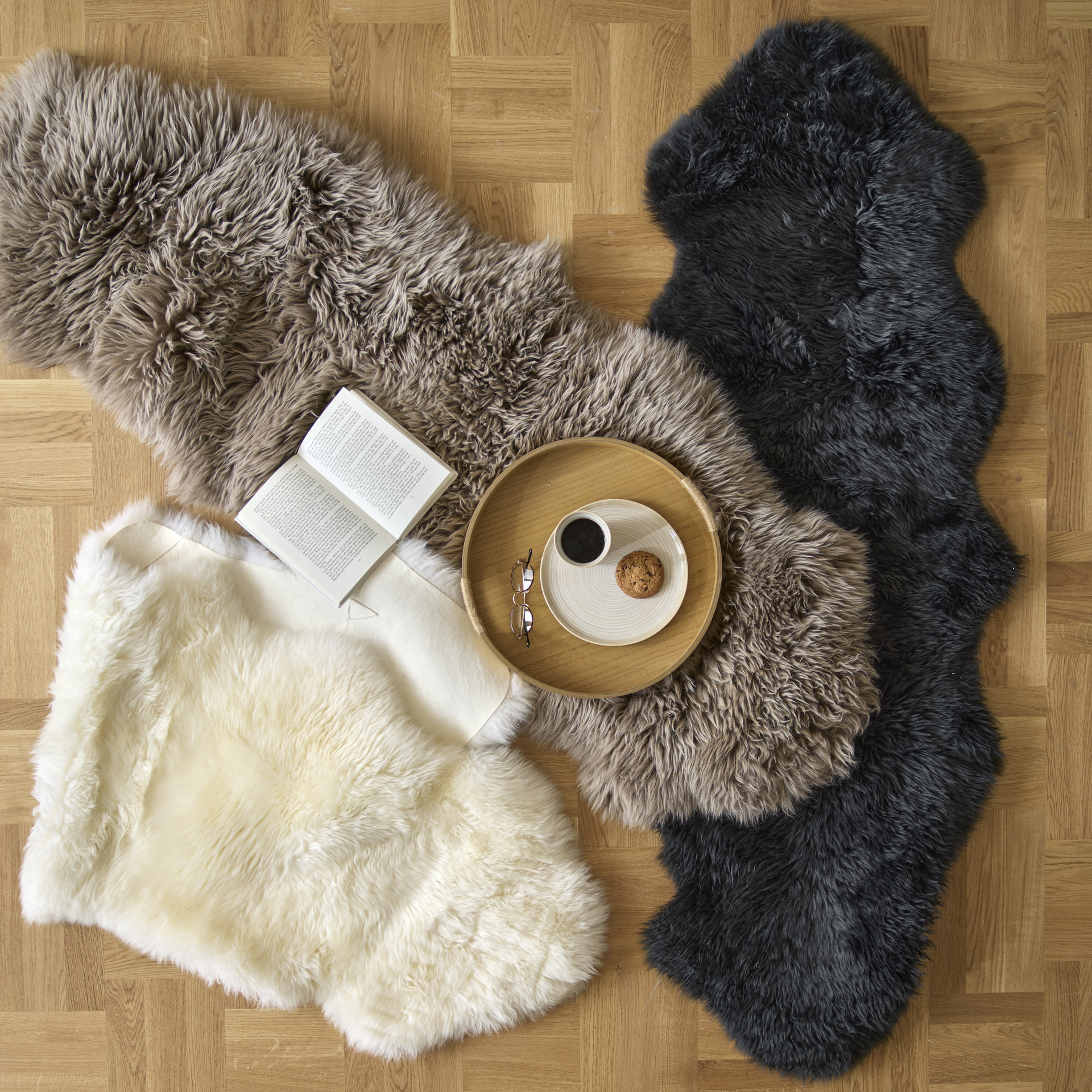 Ett vitt, ett brunt och ett svart fårskinn ligger utspridda på ett golv. På ett av fårskinnen står en bricka med fika.