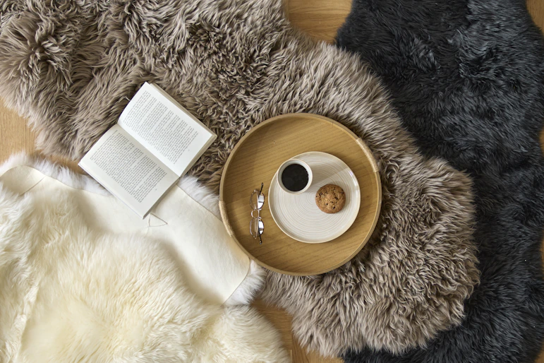 Ett vitt, ett brunt och ett svart fårskinn ligger utspridda på ett golv. På ett av fårskinnen står en bricka med fika.