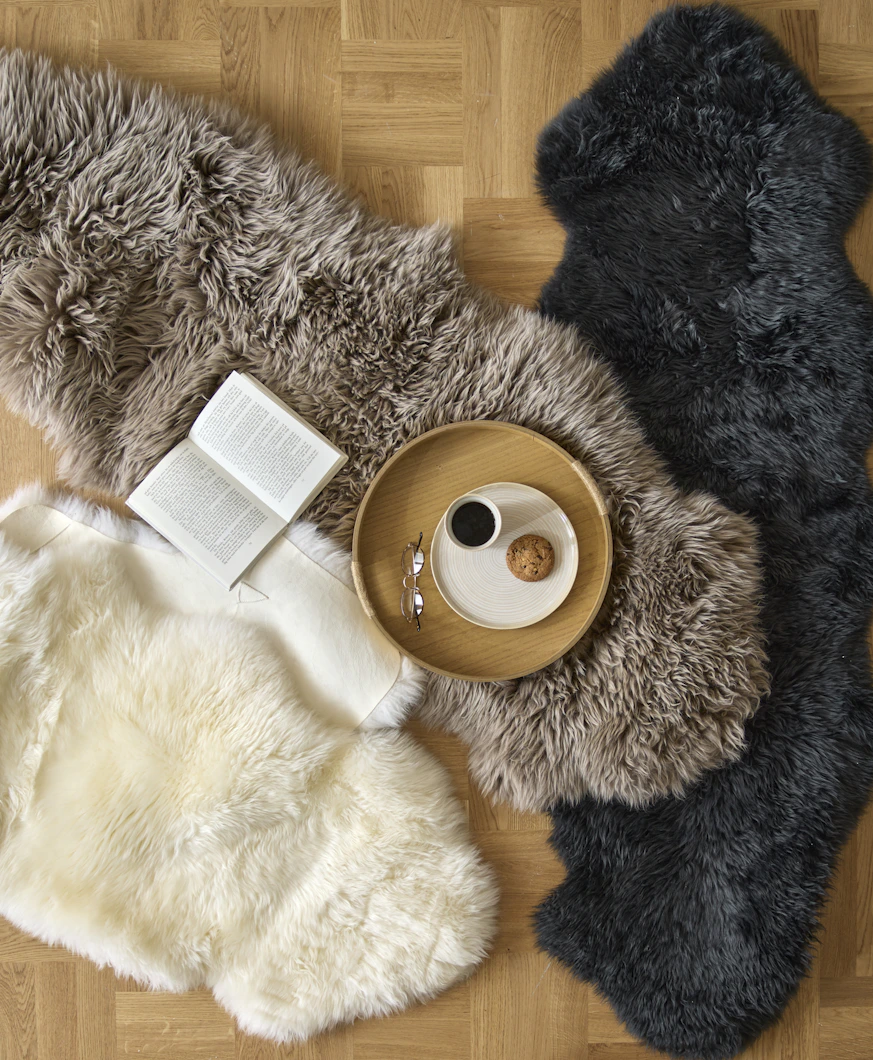 Ett vitt, ett brunt och ett svart fårskinn ligger utspridda på ett golv. På ett av fårskinnen står en bricka med fika.
