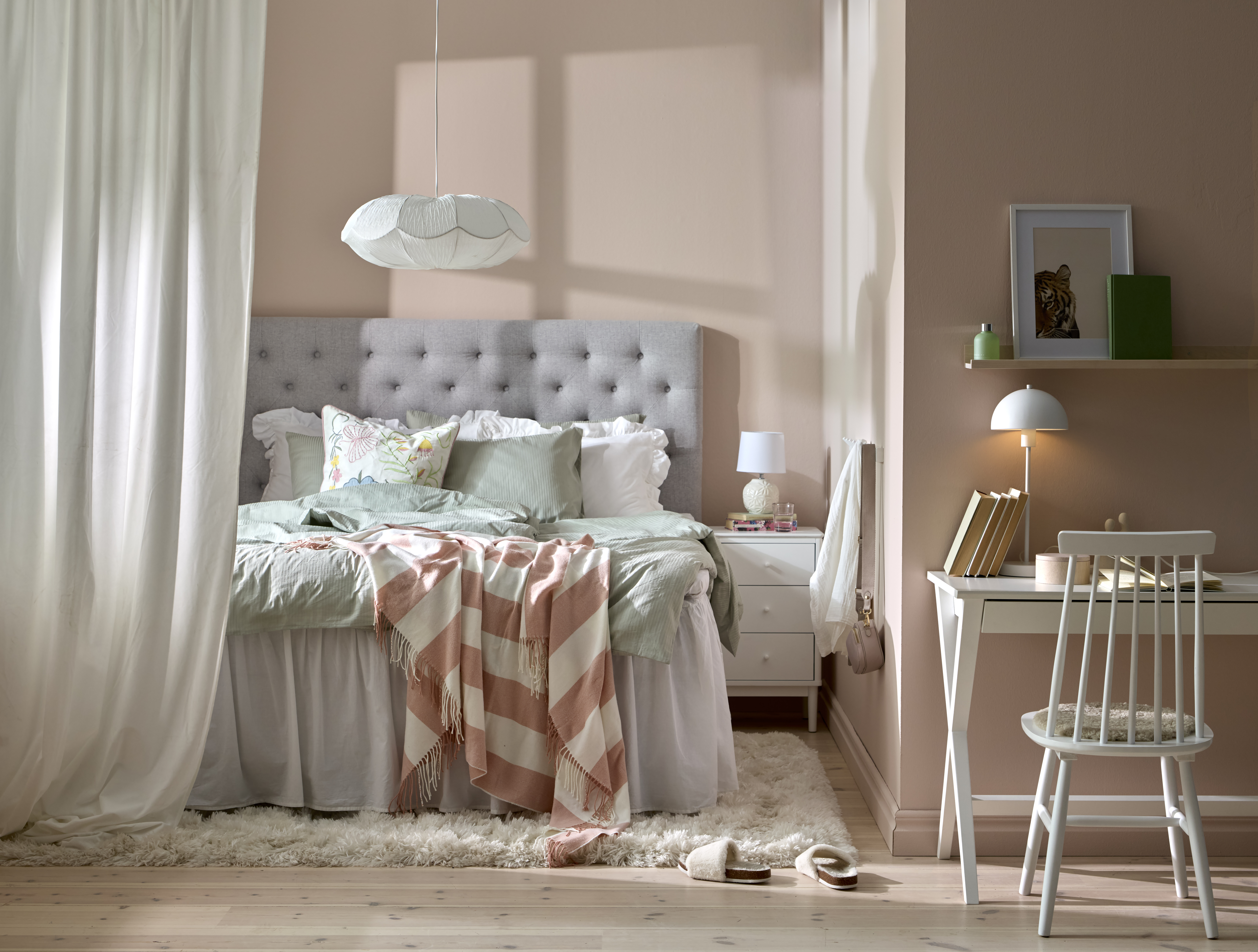 Modernt sovrum i ljusa vårliga färger, en ljusgrå säng med sänggavel och ett hemmakontor.