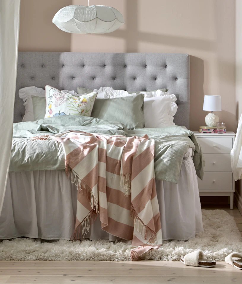 Modernt sovrum i ljusa vårliga färger, en ljusgrå säng med sänggavel och ett hemmakontor.