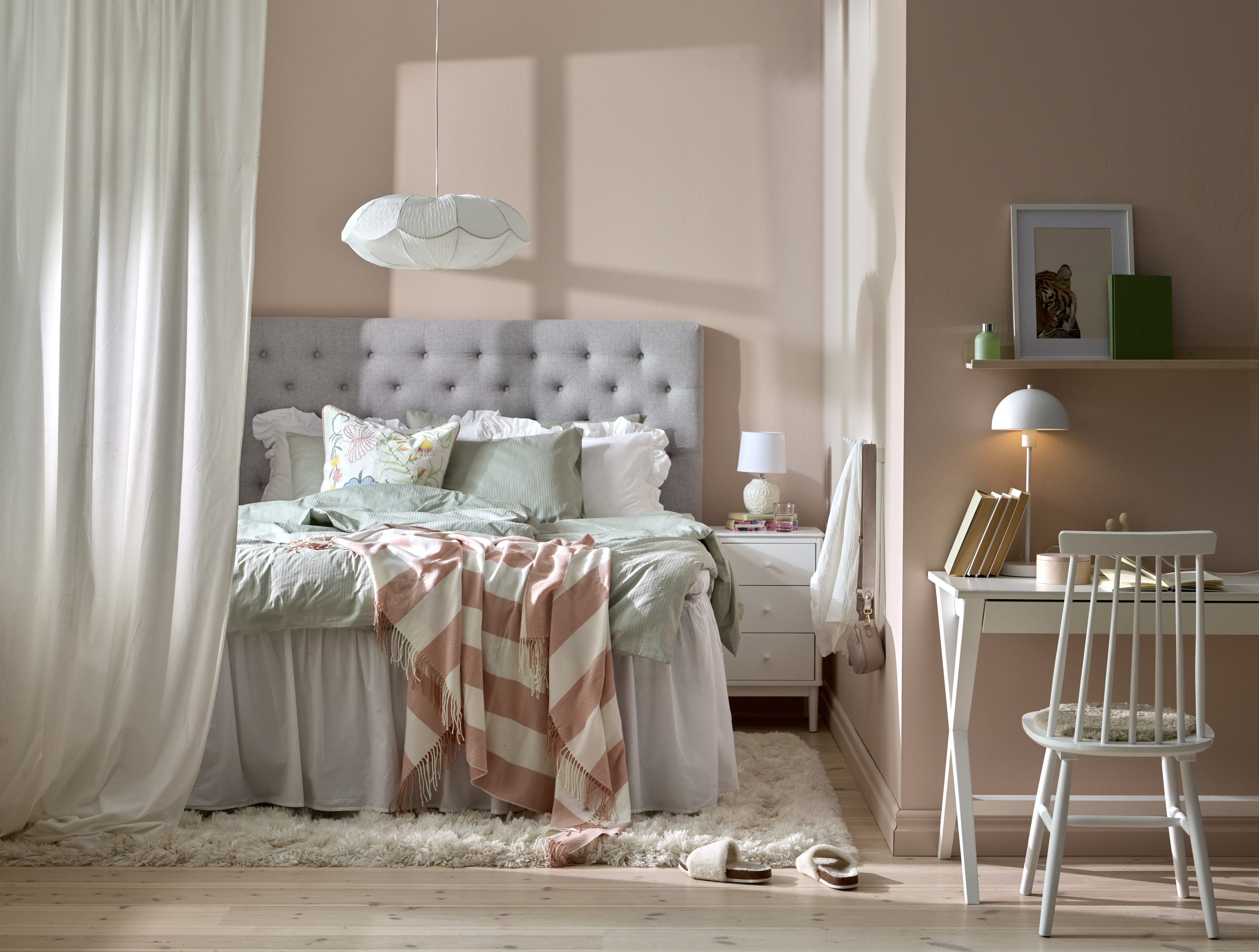 I ett rosa sovrum står et vitt skrivbord, vid skrivbordet står en vit pinnsol