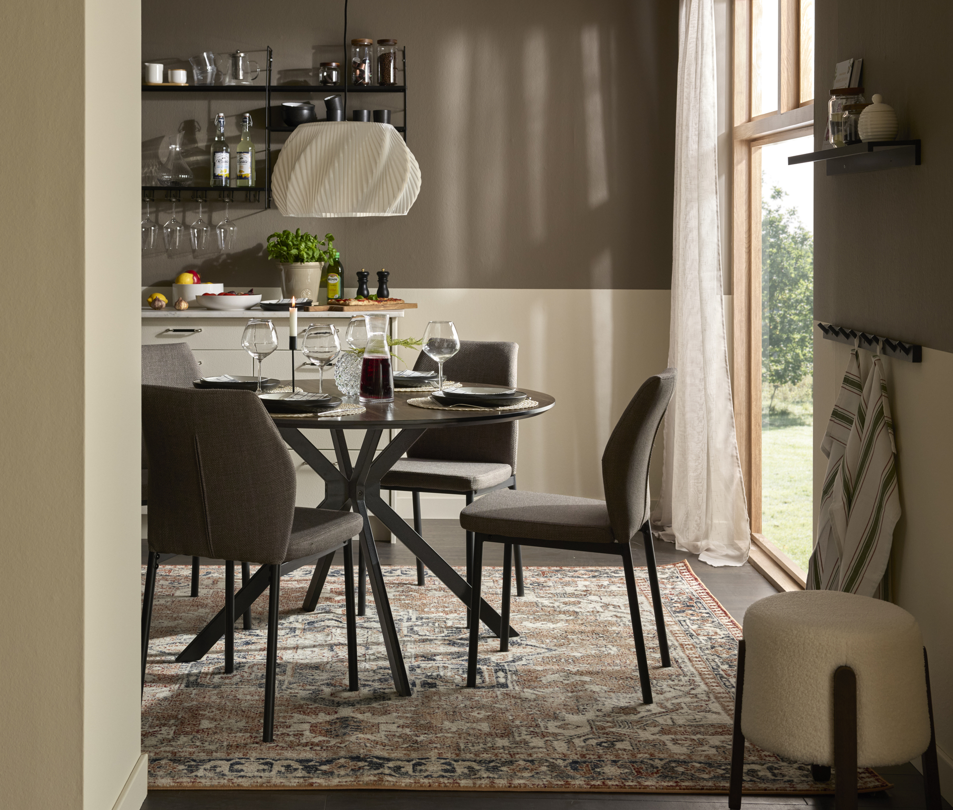 I ett kök står ett runt stilrent matbord med svart metallunderrede och fyra stolar i grått tyg och svarta metallben.