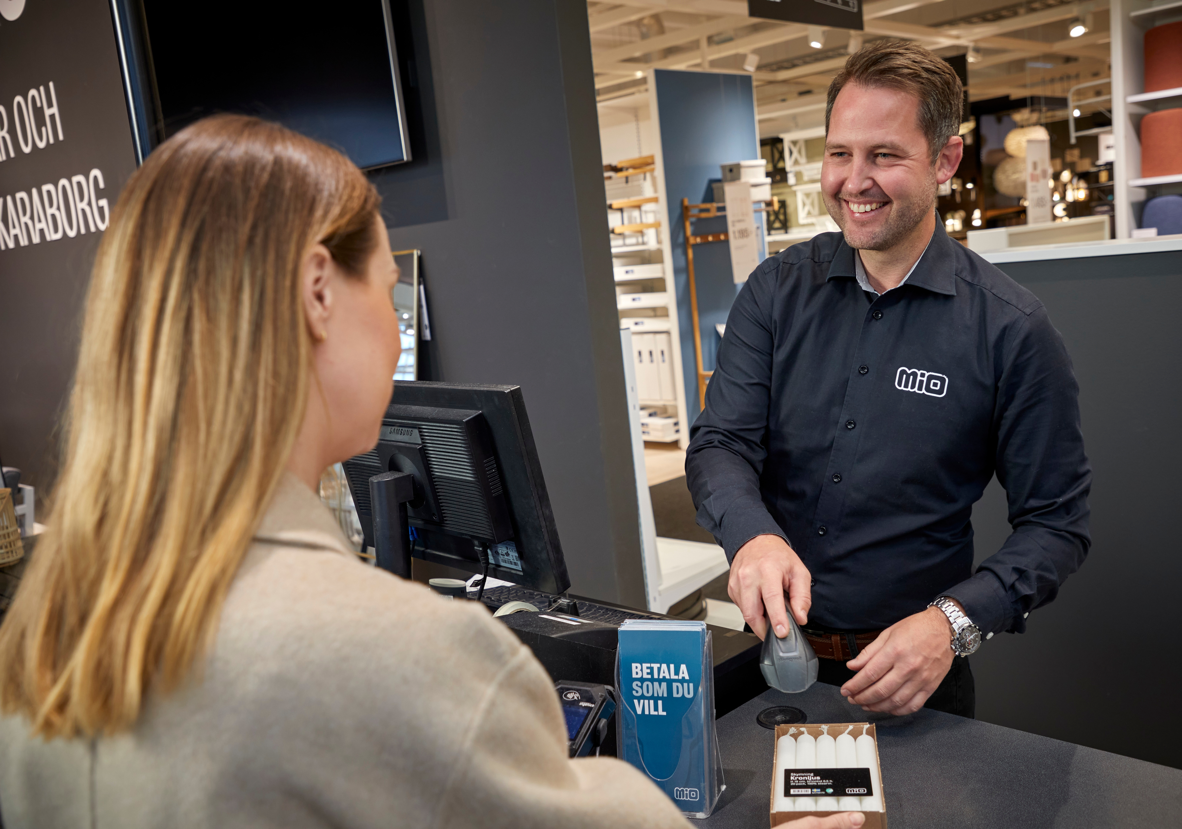 Man står bakom disk i butik och ler mot kunden.
