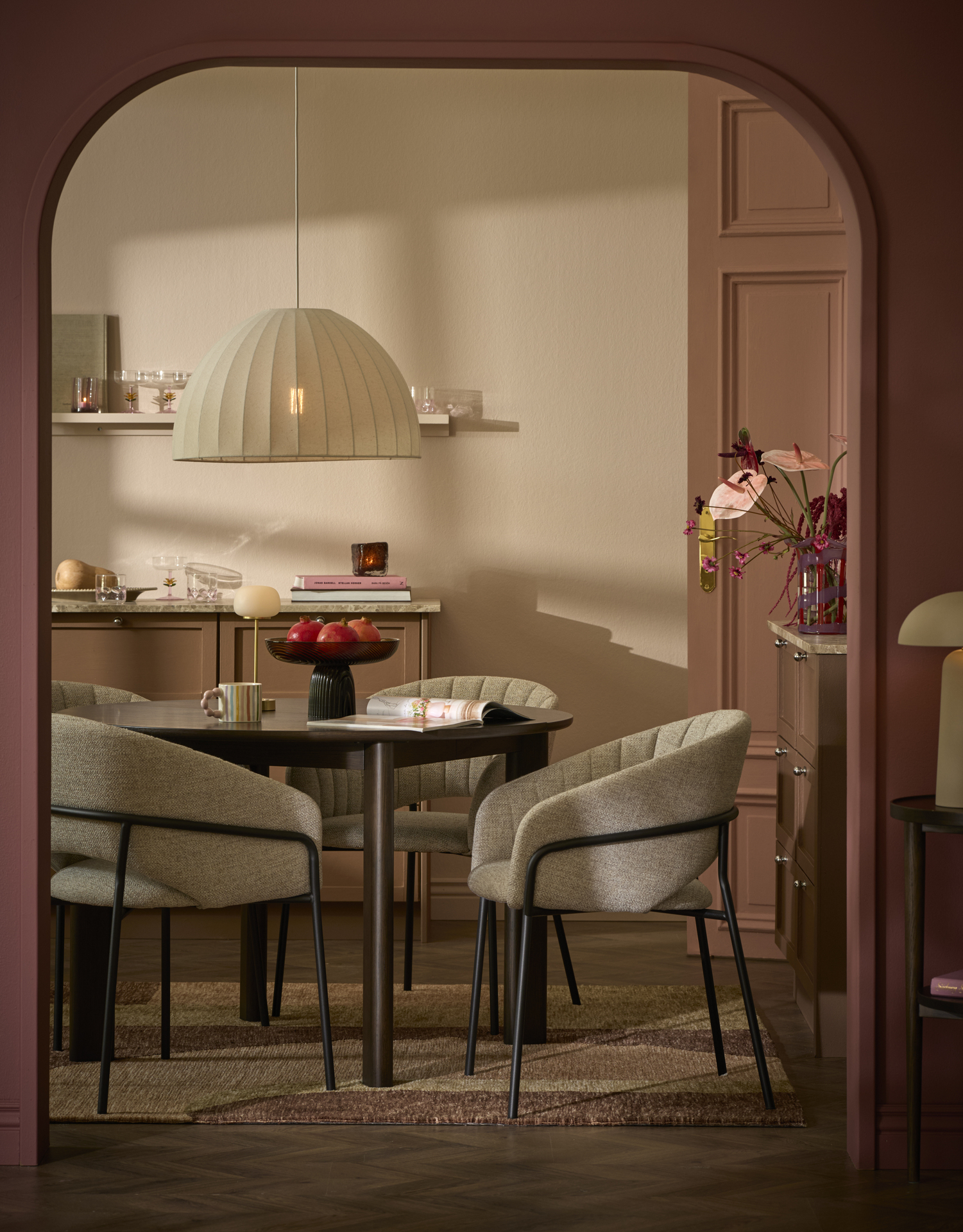 En stol i grått tyg står intill ett mörkt matbord i ett rosa matrum.