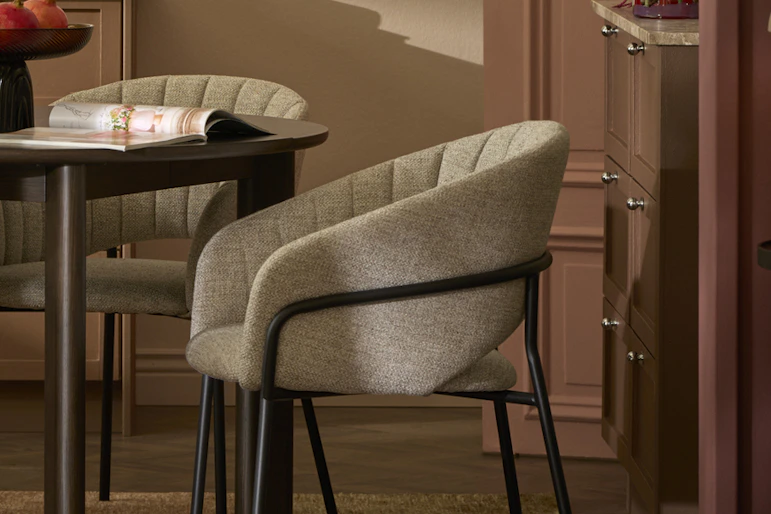 En stol i grått tyg står intill ett mörkt matbord i ett rosa matrum.