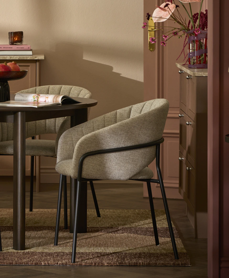 En stol i grått tyg står intill ett mörkt matbord i ett rosa matrum.