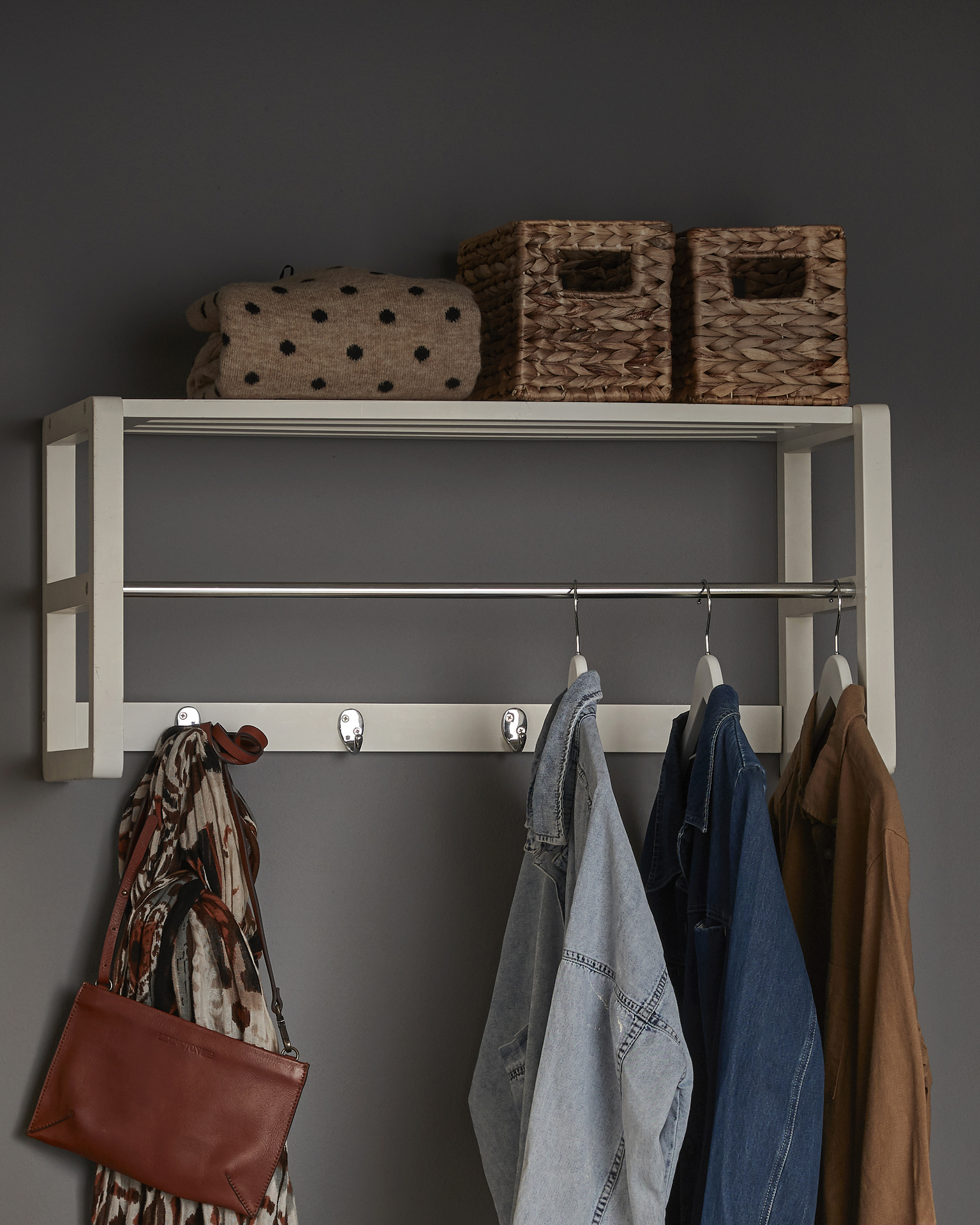 En vit hatthylla med krokar och galgar där det hänger ytterkläder.