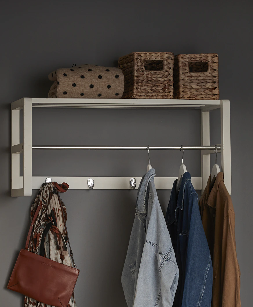 En vit hatthylla med krokar och galgar där det hänger ytterkläder.