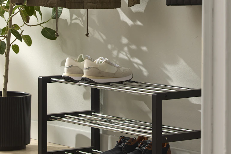 en svart skohylla står i en hall där det finns en växt och klädhängare