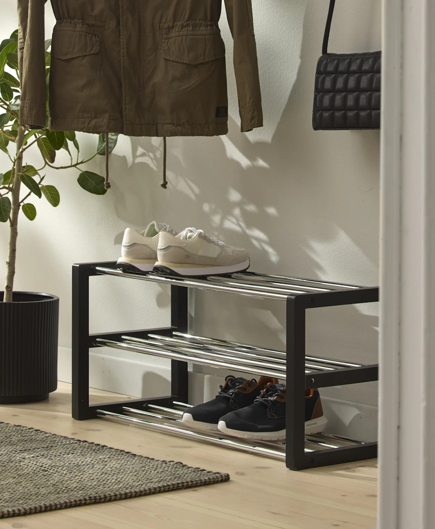 en svart skohylla står i en hall där det finns en växt och klädhängare