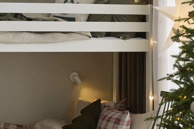 I ett sovrum står en bäddad vit våningssäng. Intill står en julgran och i fönstret hänger en julstjärna.