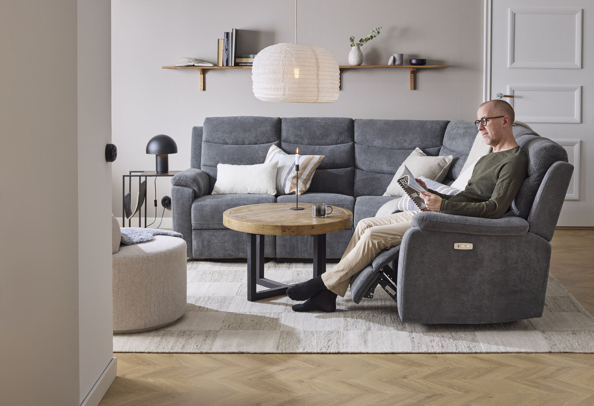I en grå hörnsoffa med reclinerfunktion sitter en man och läser