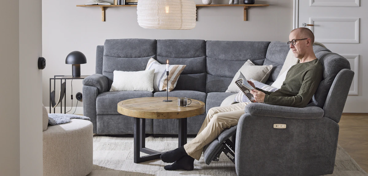 I en grå hörnsoffa med reclinerfunktion sitter en man och läser