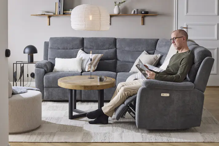 I en grå hörnsoffa med reclinerfunktion sitter en man och läser