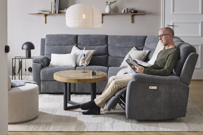 I en grå hörnsoffa med reclinerfunktion sitter en man och läser