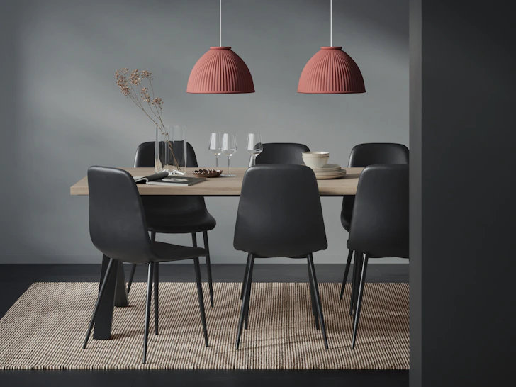 Runt ett bord med träskiva står sex stycken svata stolar i ett mörkt rum