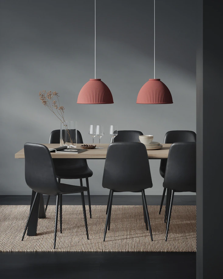 Ett matbord i trä med sex svarta stolar och två rostfärgade taklampor i ett mörkt rum