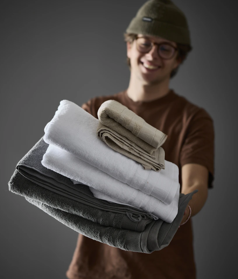 En kille håller i hopvikta handdukar i olika färger