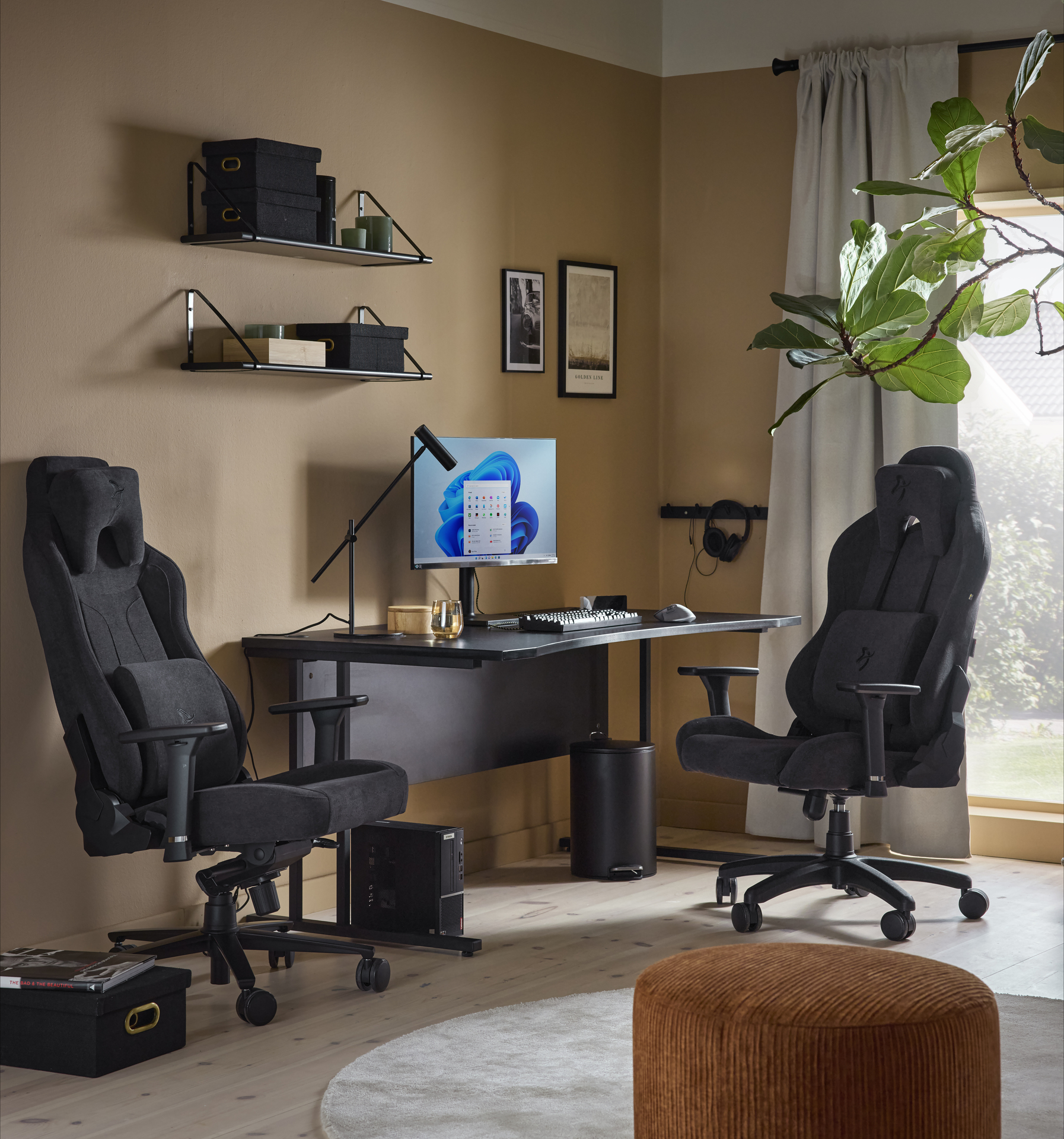 En svart gamingstol står framför ett svart skrivbord i ett rum med varmt gula väggar.