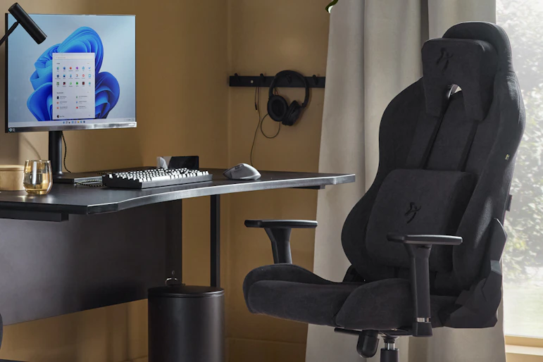 En svart gamingstol står framför ett svart skrivbord i ett rum med varmt gula väggar.