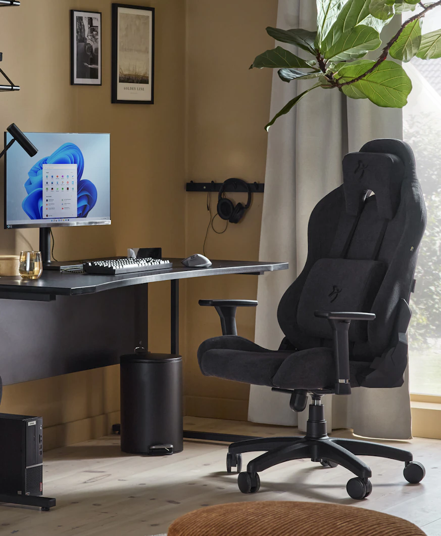 En svart gamingstol står framför ett svart skrivbord i ett rum med varmt gula väggar.