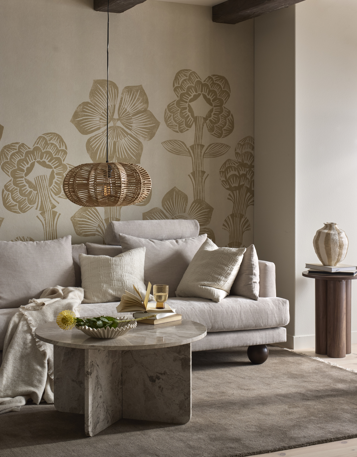 En beige soffa står i ett vardagsrum med beiga väggar. Framför soffan finns ett runt soffbord i sten och en beige matta.