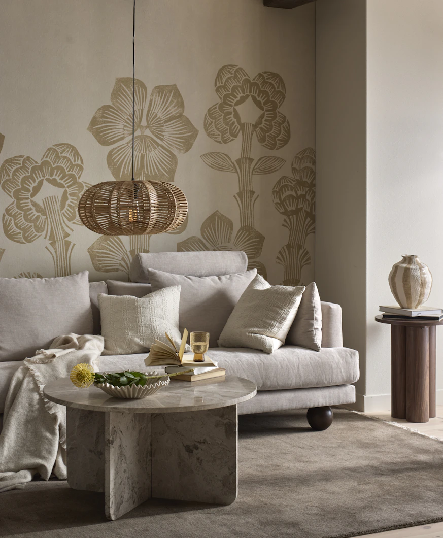 En beige soffa står i ett vardagsrum med beiga väggar. Framför soffan finns ett runt soffbord i sten och en beige matta.