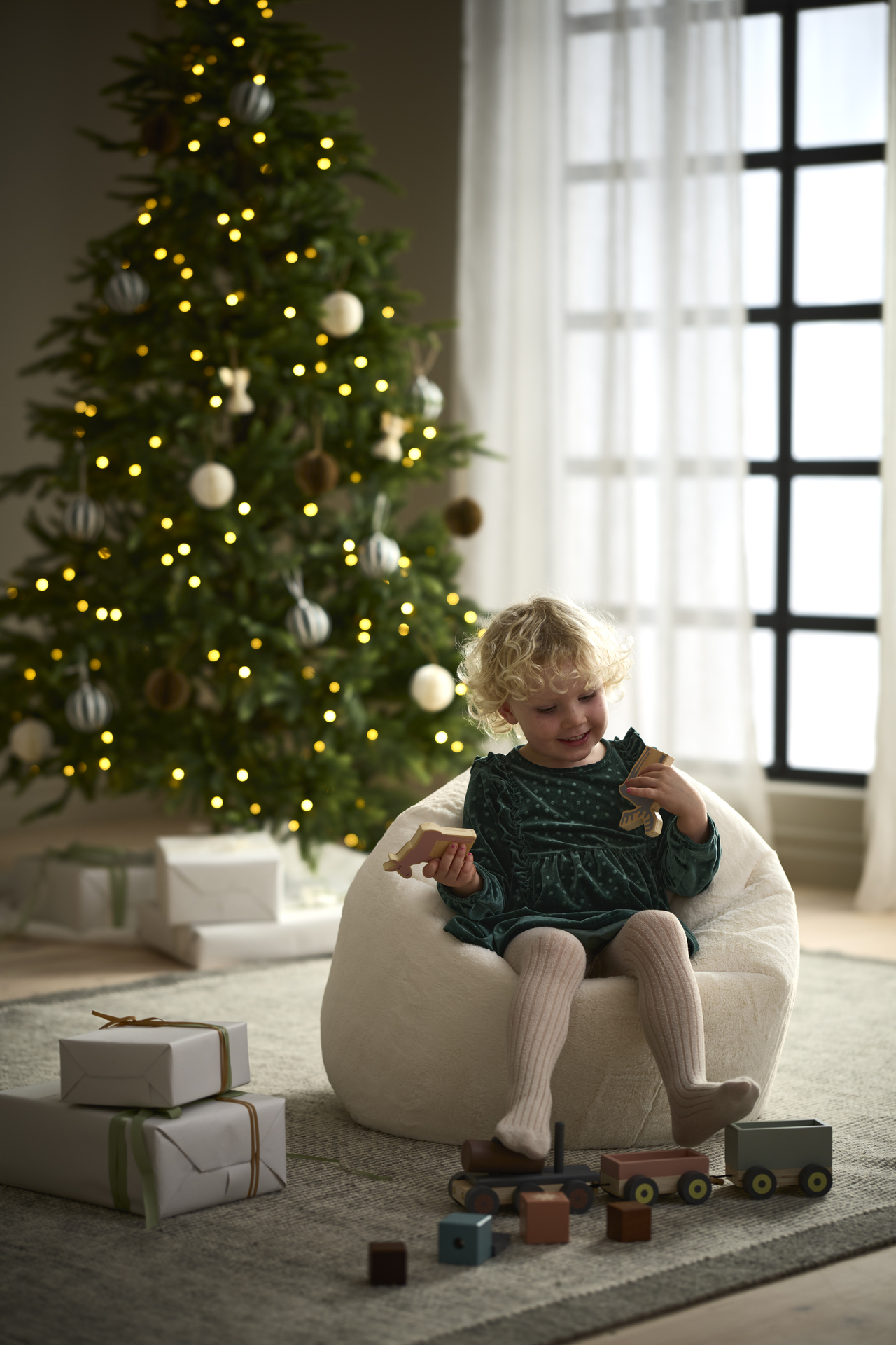 ett barn sittandes i en sittsäck framför en julgran
