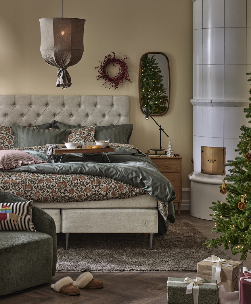 ett sovrum med en stor beige säng, en taklampa i tyg och en vit kakelugn i hörnet av rummet